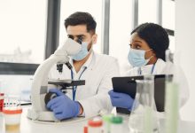 Pesquisadores analisam amostras ao microscópio e fazem anotações em um laboratório moderno.