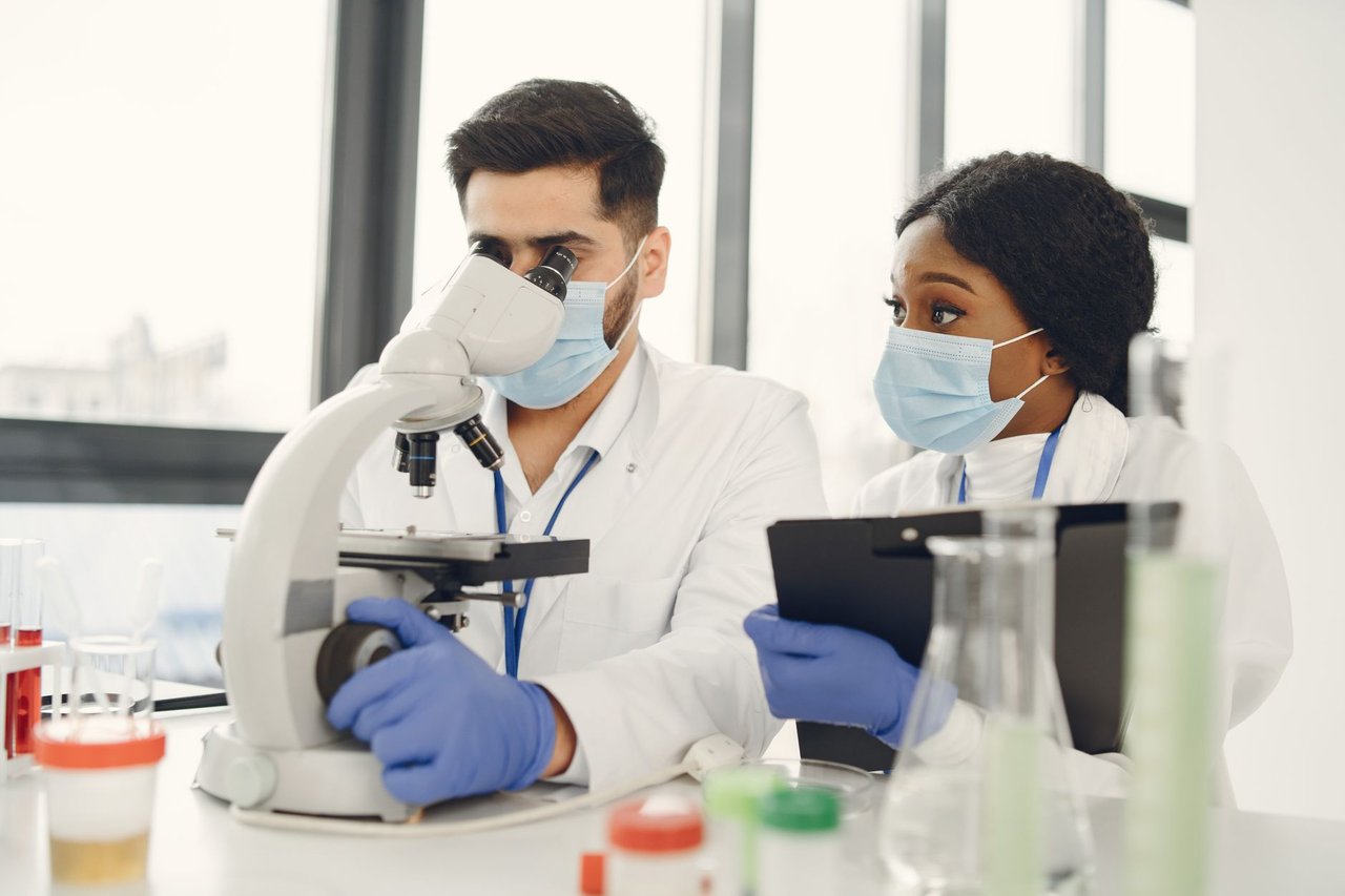 Pesquisadores analisam amostras ao microscópio e fazem anotações em um laboratório moderno.