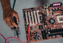 Engenheiro solda componentes de uma placa-mãe em um laboratório de tecnologia.