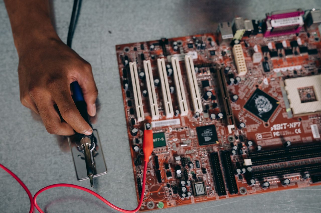 Engenheiro solda componentes de uma placa-mãe em um laboratório de tecnologia.