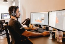 Profissional usando fones de ouvido trabalha diante de um computador com dois monitores em um escritório moderno.