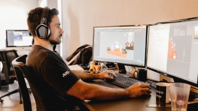 Profissional usando fones de ouvido trabalha diante de um computador com dois monitores em um escritório moderno.