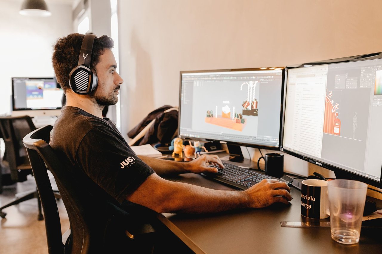 Profissional usando fones de ouvido trabalha diante de um computador com dois monitores em um escritório moderno.