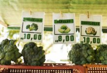 Hortaliças variadas expostas em um mercado, com etiquetas de preço visíveis.