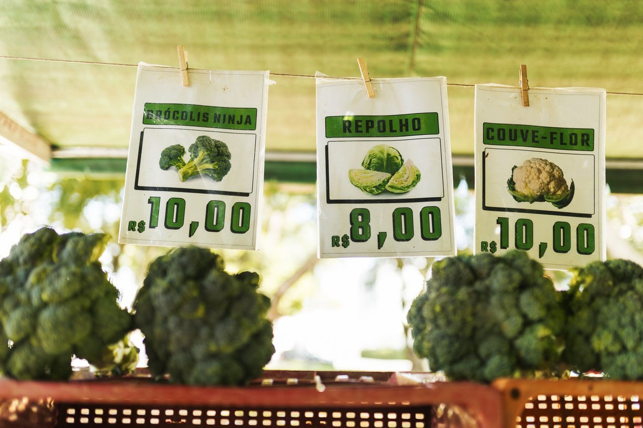 Hortaliças variadas expostas em um mercado, com etiquetas de preço visíveis.