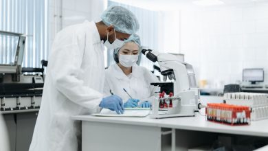 Dois pesquisadores trabalham juntos em um laboratório, utilizando microscópios e outros equipamentos científicos.