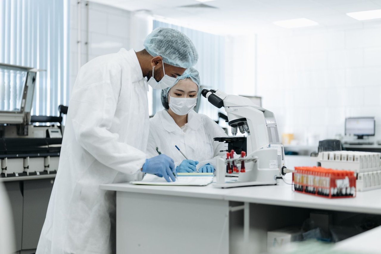 Dois pesquisadores trabalham juntos em um laboratório, utilizando microscópios e outros equipamentos científicos.